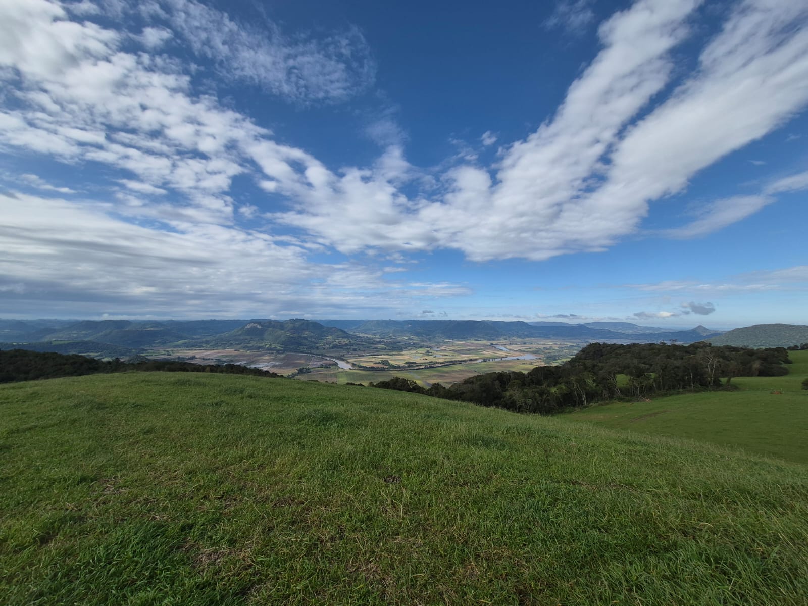 Vista panorâmica do vale da Quarta Colônia, com campo verde, rios, morros e céu aberto