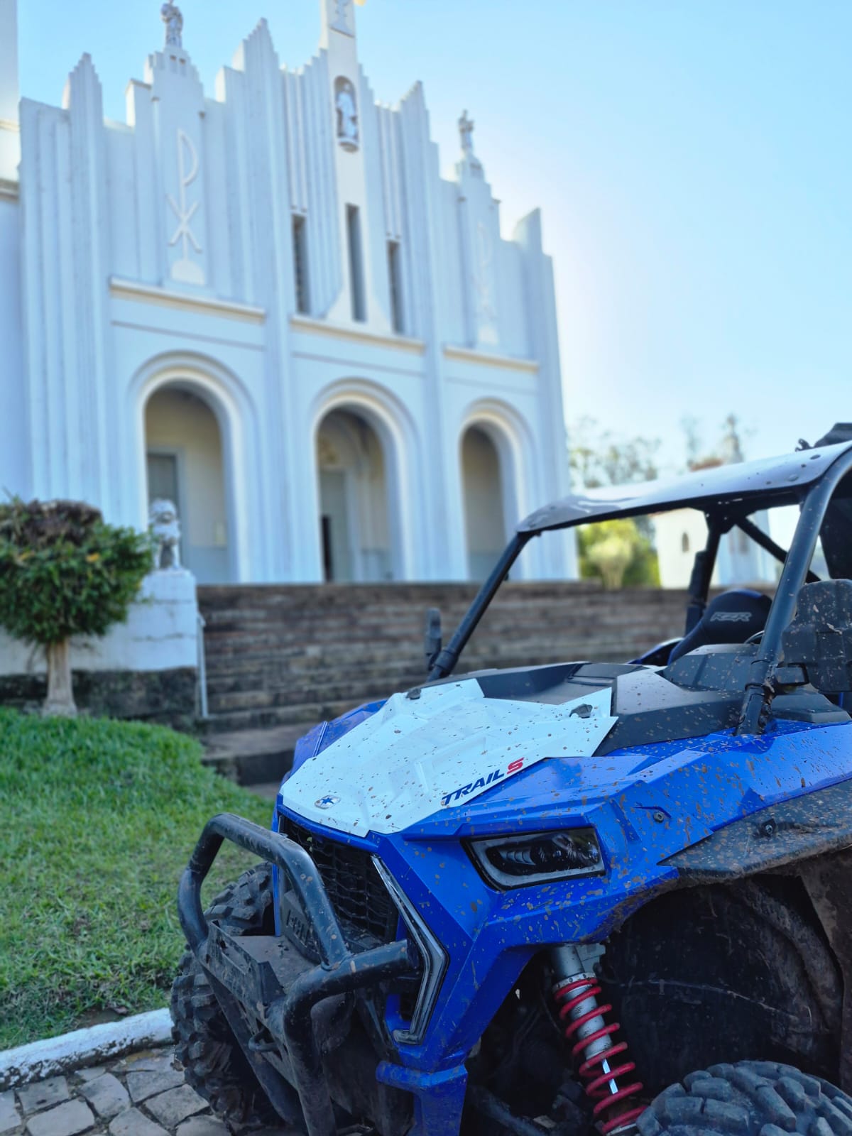 Polaris RZR azul com marcas de barro estacionado diante de uma igreja branca