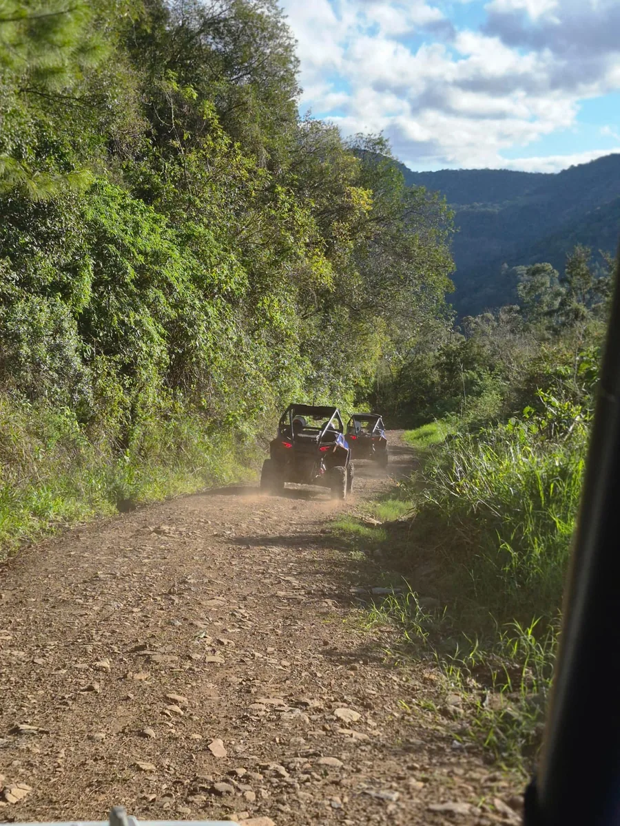 Comboio de UTVs levantando poeira numa estrada de chão entre morros
